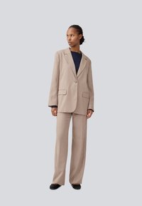 Beige tailored blazer with notch lapels, single button, and two front pockets, paired with matching wide-leg trousers and dark top.