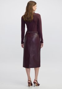 Bordeaux leren midi-rok met een gladde textuur, een split aan de achterkant en een aansluitende tailleband. Gekozen in combinatie met een langemouw maroon top en hakken.