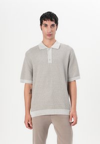 Kortermet polo laget av lett, teksturert grå strikket stoff. Har en kontrasterende lys grå krage og en frontplacket med tre knapper.