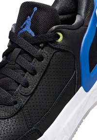 Close-up van een zwarte sportieve sneaker met geperforeerde bovenkant, zwarte veters, blauwe details en een witte zool met een blauw Jumpman-logo op de tong.