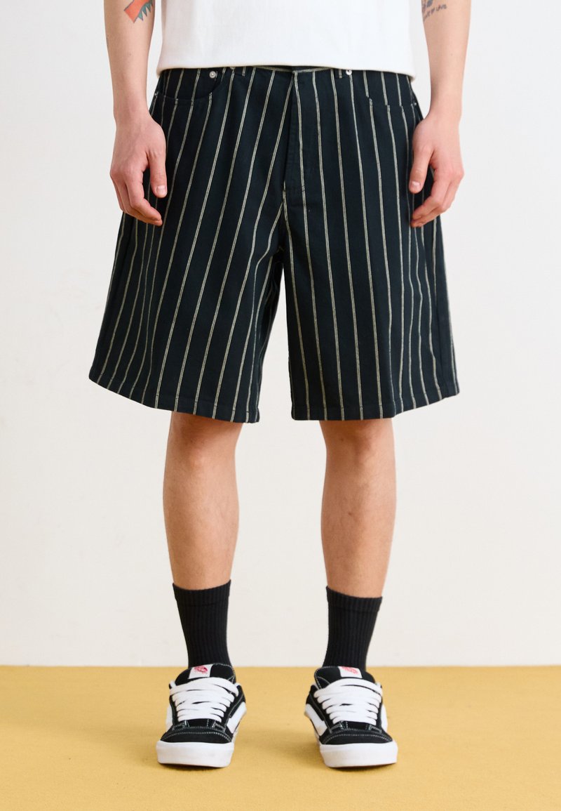 Black striped shorts feature a relaxed fit with a straight leg, made of cotton fabric with a smooth texture. Small pockets are visible.