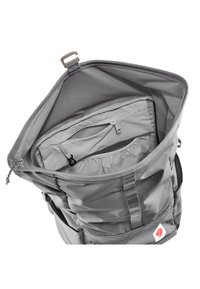 Zaino grigio in materiale nylon testurizzato. Apertura superiore che rivela un ampio interno e una tasca con zip per l'organizzazione. Spallacci regolabili.