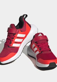 Červené a růžové sportovní boty s prodyšným svrškem, bílými pruhy a černou gumovou podrážkou. Obsahují strap na suchý zip a klasické šněrování.