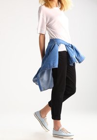 Light gray short-sleeve shirt, tied denim jacket at the waist, black tapered pants, and light blue sneakers with beige laces.