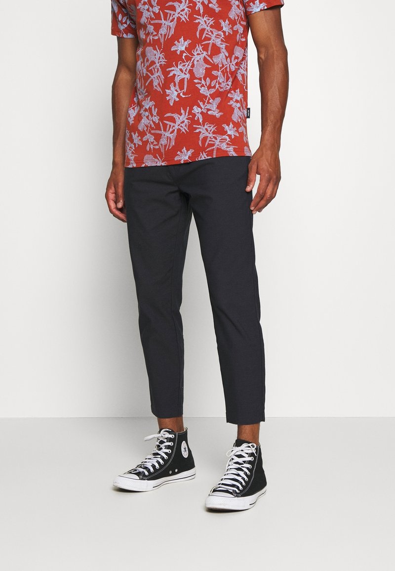 Red short-sleeve shirt with white floral pattern, paired with dark fitted pants and black high-top sneakers with white soles.