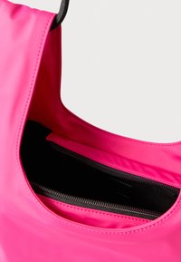 Różowa torba na ramię z gładką, matową powierzchnią i czarną wewnętrzną kieszenią na suwak. Zaokrąglone, szerokie otwarcie z solidnym uchwytem.