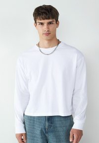 Biała koszula z długim rękawem i okrągłym dekoltem, o luźnym kroju. W połączeniu z jasnoniebieskimi dżinsami. Akcent w postaci srebrnego naszyjnika.