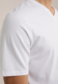 Witte katoenen V-hals T-shirt met korte mouwen. Soepele textuur, casual ontwerp en strakke lijnen. Naaddetails bij de mouwzoom.