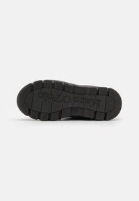 Semelle de chaussure en caoutchouc noir avec des nervures et des rainures texturées ; comporte un logo estampé en lettres majuscules sur la surface.