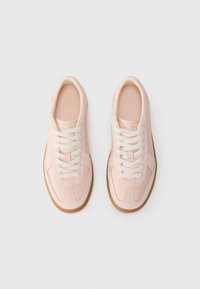 Sneaker rosa chiaro con tomaia strutturata, lacci bianchi e suola in gomma marrone. Presenta un sottile dettaglio del logo sulla linguetta.