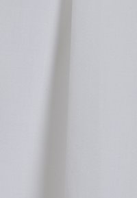 Tessuto di cotone bianco con una superficie liscia e leggermente texturizzata, caratterizzato da un motivo uniforme e privo di hardware o accenti visibili.