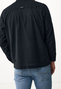 Black, lightweight button-up shirt with long sleeves and a rectangular back yoke. Features a subtle tag at the neck and stitched accents.