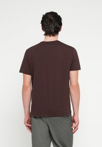 Pruun lühikeste varrukatega T-särk, mis on valmistatud pehmest kangast, klassikalise lõike ja ümara kaelusega. Lihtne disain, puuduvad nähtavad mustrid või aktsendid.