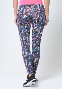 Leggings multicolori con un motivo geometrico in blu, nero e viola. Presentano un cinturino rosa e scarpe da ginnastica nere.