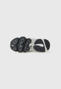 Semelle de sneaker avec une semelle extérieure en caoutchouc noir texturé, des rainures pour l'adhérence, et une semelle intermédiaire blanche avec des éléments de marque et des accents de design visibles.