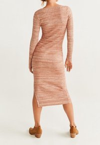 Abito midi a maniche lunghe a coste in rosa polveroso con una silhouette aderente e spacco laterale, realizzato in tessuto a maglia testurizzata. Abbinato a tacchi marroni.