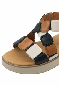 Bruine en zwarte leren sandaal met vierkante patches in tan, zwart en wit. Gevoerde binnenzool met een lichtgekleurde buitenzool.