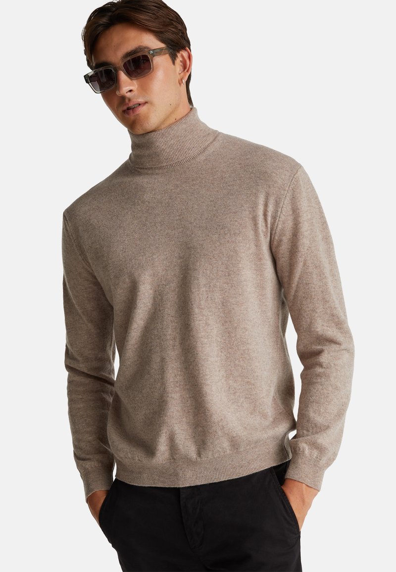 Hellbrauner, gestrickter Rollkragenpullover mit langen Ärmeln und gerippten Bündchen, kombiniert mit schwarzen Hosen. Glatte Textur, lässiges Design.