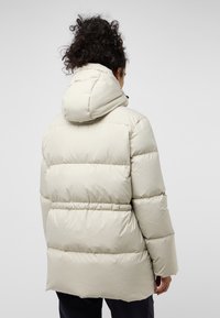 Beige gewatteerde jas met capuchon, voorzien van horizontaal doorgestikte secties, elastische cuffs en een ontspannen pasvorm. Glad, glanzend buitenmateriaal.