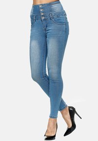 Jeans skinny de mezclilla azul de tiro alto con cierre de botón, cinco bolsillos y un diseño ajustado. Tejido texturizado con ligero desgaste.