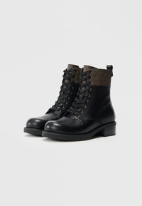 Bottines en cuir noir avec un dessus en cuir texturé marron, bouts ronds, œillets dorés et un petit talon épais. Présente des lacets et une poignée.