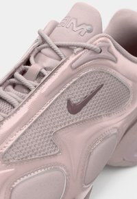 Ροζ ανοιχτό αθλητικό παπούτσι Nike με επάνω μέρος από υφασμάτινο πλέγμα με υφή, γυαλιστερές λεπτομέρειες και αντίθετο σκοτεινό ροζ λογότυπο swoosh στο πλάι.