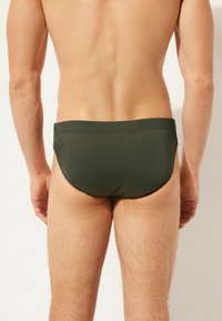 Männliche Schwimmslips in Olivgrün, aus glattem Material. Mit einem tief sitzenden Schnitt, einem elastischen Bund und minimalen Nahtdetails.