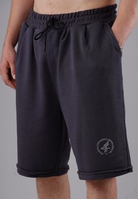 Dunkelgraue Sportshorts aus einem weichen, dehnbaren Stoff. Mit einem elastischen Bund, seitlichen Taschen und einem Logo am unteren Bein.