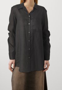 Chemise en lin noire à boutons avec manches longues, une poche poitrine et une coupe décontractée. Dotée d'un col classique et d'un léger éclat.