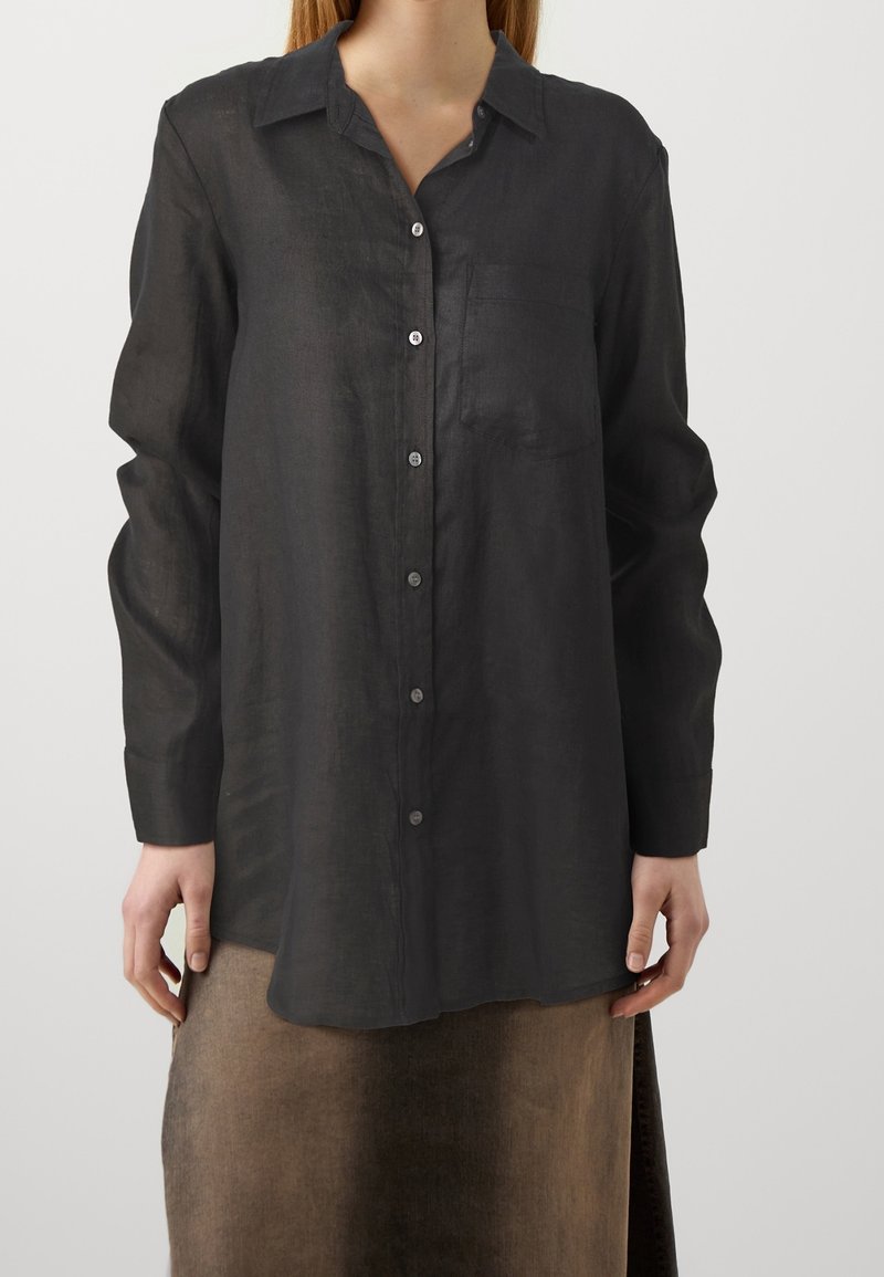 Chemise en lin noire à boutons avec manches longues, une poche poitrine et une coupe décontractée. Dotée d'un col classique et d'un léger éclat.