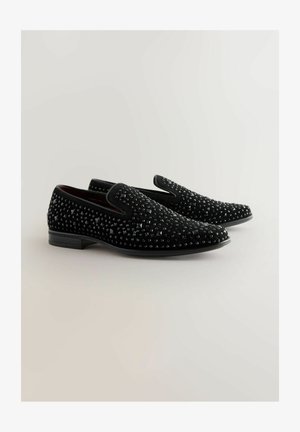 Černé nazouvací boty s texturovaným svrškem, který zdobí malé, lesklé cvočky. Hladký, zaoblený špička a nízký plochý podpatek. Moderní design.