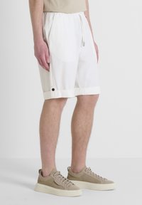 Pantaloni corti bianchi con cordoncino, dal fit rilassato, caratterizzati da un dettaglio con bottone nero a contrasto all'orlo. Realizzati in tessuto leggero.