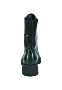 Bota de tobillo verde de cuero con suela negra gruesa, cremallera lateral y acentos texturizados en el talón. La vista trasera muestra un acabado suave.