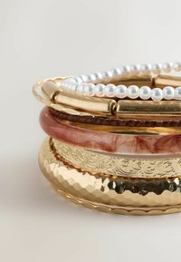 Gold and pink bracelets stacked together. Includes textured gold with a hammered finish, smooth pink, and pearl-like beads.