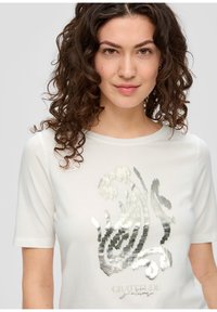 Witte t-shirt met korte mouwen en een zilverkleurig textuurontwerp aan de voorkant, met het woord "GRATITUDE" in een stijlvolle lettertype.