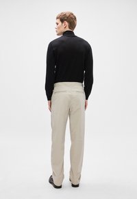 Μαύρη μπλούζα με μακριά μανίκια και ανοιχτό μπεζ παντελόνι, και τα δύο εφαρμοστά. Το παντελόνι έχει μαλακή υφή και ελαστική μέση με διακριτική λεπτομέρεια στο πίσω μέρος.