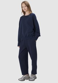 Navyblauw sweatshirt en bijpassende joggingbroekset gemaakt van zachte stof. Het sweatshirt heeft een losse pasvorm; de joggingbroeken hebben zijzakken. Zilveren sneakers.