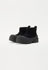 Botine negre până la gleznă, cu un superior texturat și talpă din cauciuc neted, având un vârf rotunjit și o bandă pentru a fi ușor de îmbrăcat.