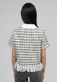 Haut à manches courtes en tweed blanc et noir avec un ourlet à franges et un col, présentant un motif texturé.