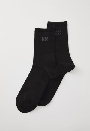 Par čarapa bez uzorka, crne boje, do gležnja, s "HUGO" logotipom u tamnosivoj boji blizu rubova, prikazane ravno na bijeloj pozadini.
