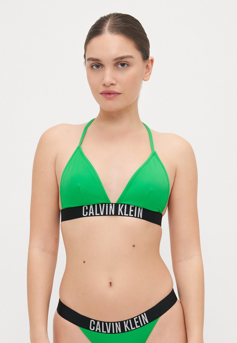 Lysegrønn bikini-sett med trekantet BH med tynne stropper og en svart stropp merket "CALVIN KLEIN"; matchende bikini-bunn med svart stropp.