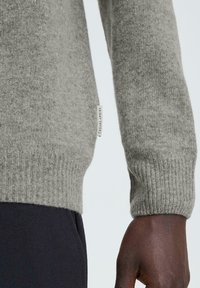 Grå stickad tröja med ribbad mudd, tillverkad av mjukt material. Har en liten märkesetikett på sidan nära fållen.