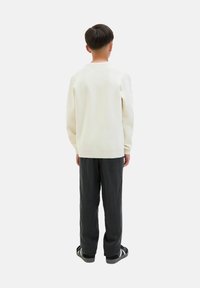 Cream-colored sweater with ribbed cuffs, paired with loose-fitting, dark gray trousers. The outfit is completed with black and white sandals.