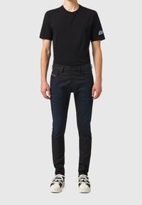 Svart t-shirt med kort ärm, i kombination med mörkblå jeans som har framfickor och subtil blekning. Skor: mönstrade sneakers.