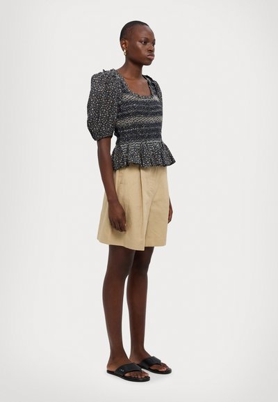 Crop top noir à motif floral, avec des manches ballon, un corsage texturé et un ourlet peplum, associé à un short plissé beige clair et des sandales à slides noires.