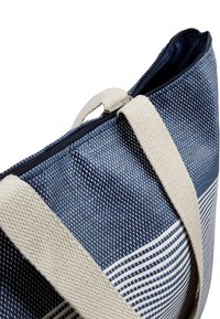 Gestreifte Stofftasche in Marineblau und Weiß, mit einem strukturierten Gewebe, cremefarbenen Baumwollgriffen und einem Reißverschluss.