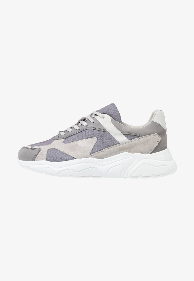 Sneakers gris avec une combinaison de cuir suédé et de mesh, une semelle en caoutchouc blanc, des accents texturés et un design sportif avec fermeture à lacets.