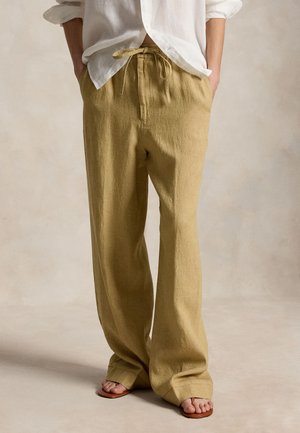 Άτομο που φορά χαλαρά μπεζ παντελόνια με κορδόνι στη μέση, λευκό πουκάμισο με μακριά μανίκια που έχει τυλιχτεί, και καφέ σανδάλια με ανοιχτά δάχτυλα, στέκεται όρθιο.