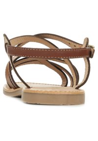 Sandalias de cuero marrón con múltiples tiras delgadas que se intersectan, suela plana y detalles de costura. Plantilla de color marrón claro con textura suave.