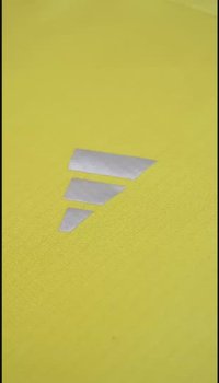 Gelbes Sportgewebe mit einer strukturierten Oberfläche und einem reflektierenden silbernen Logo in dreieckiger Form in der Mitte.